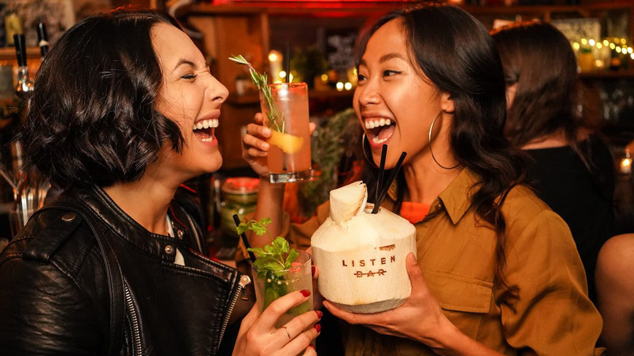 Zwei Frauen mit alkoholfreien Drinks in einer Bar lachen einander an.