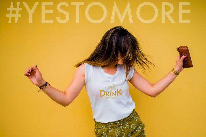 Frau mit Drink Revolution-Shirt tanzt unter dem Hashtag "Yes to more"