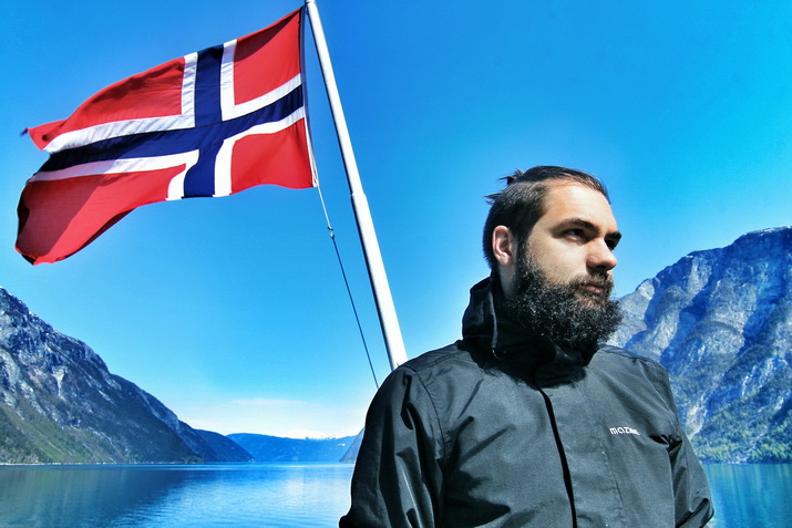 Mann vor norwegischer Flagge im Fjord