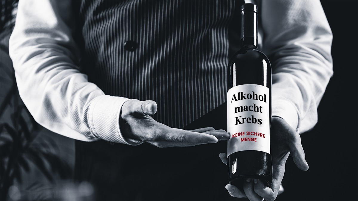 Kellner präsentiert Flasche mit Aufschrift "Alkohol macht Krebs. Keine sichere Menge"