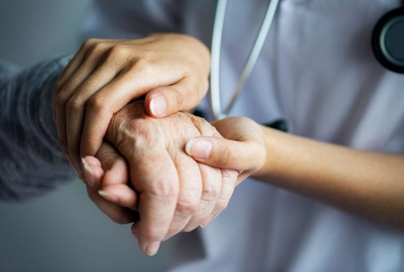 Pflegeperson hält Hand eines Patienten