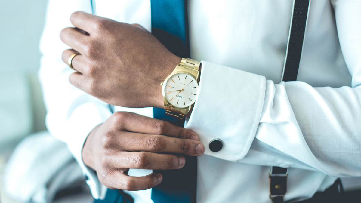 Mann mit weißem Hemd und teurer Uhr richtet seinen Manschettenknopf