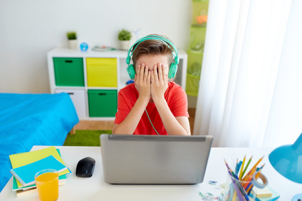 Junge vor Laptop hält sich die Hände vor die Augen