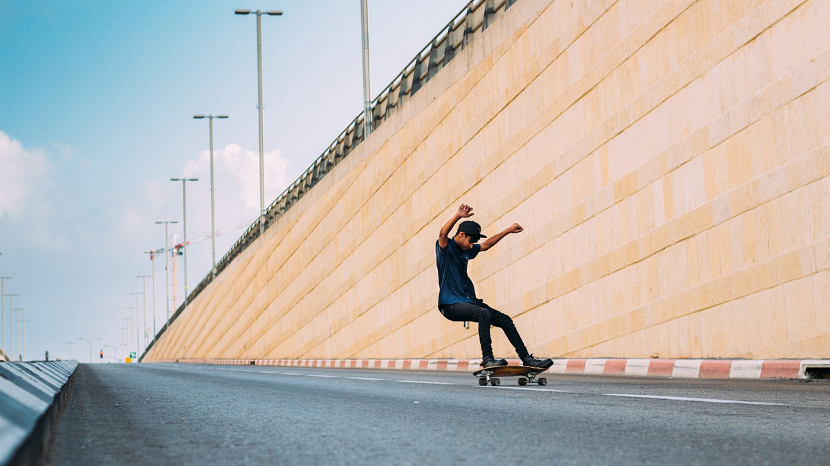 Junger Mann auf Skateboard fährt abschüssige Straße hinunter