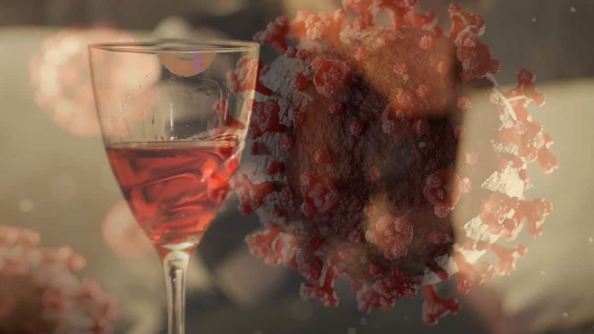Gefülltes Weinglas, unscharf im Hintgerund Frau auf Sofa, die das Gesicht verbirgt. Das ganze Bild wird durch ein semitransparentes Bild von Coronaviren überdeckt.