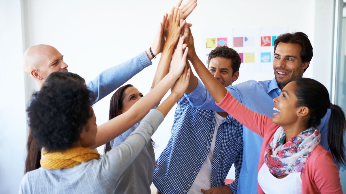 Sechs Personen in einem Zimmer klatschen ihre Hände zum High Five aneinander