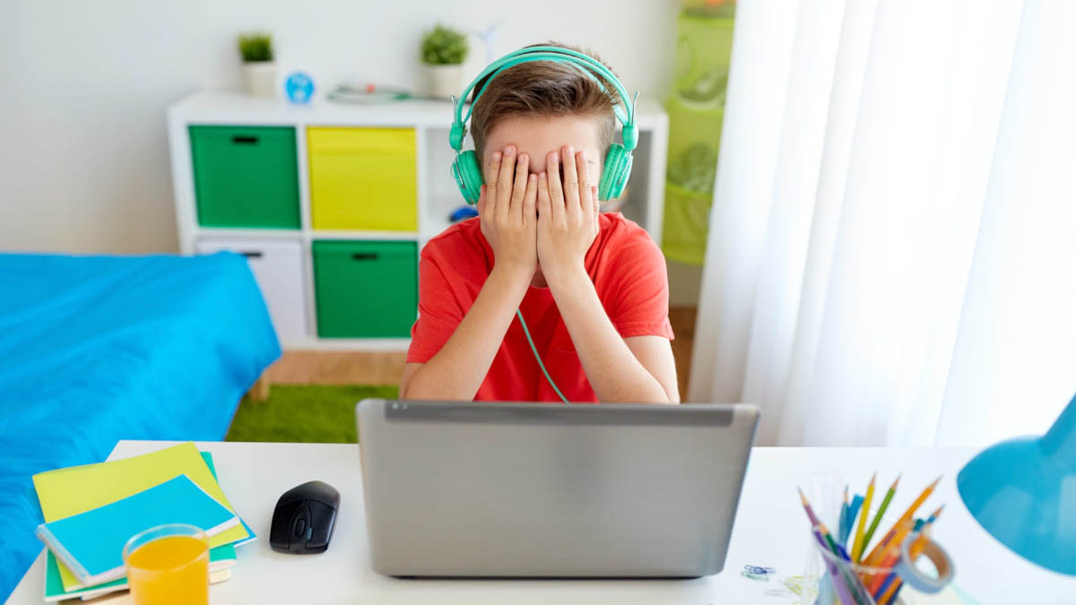 Junge mit Kopfhörern vorm Laptop hält sich die Hände vor die Augen