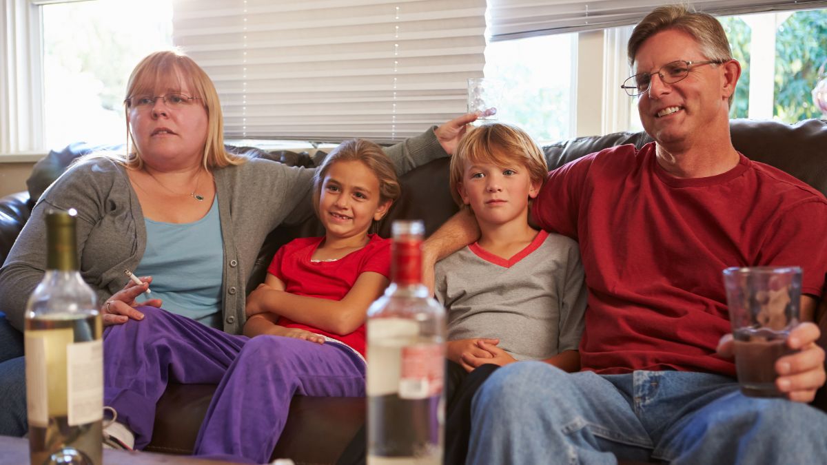 Kinder sitzen mit Eltern auf Couch, die Alkohol trinken und rauchen