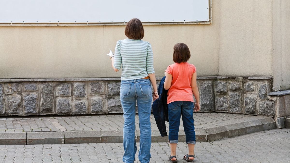 Frau und Mädchen schauen auf eine Plakatwand.