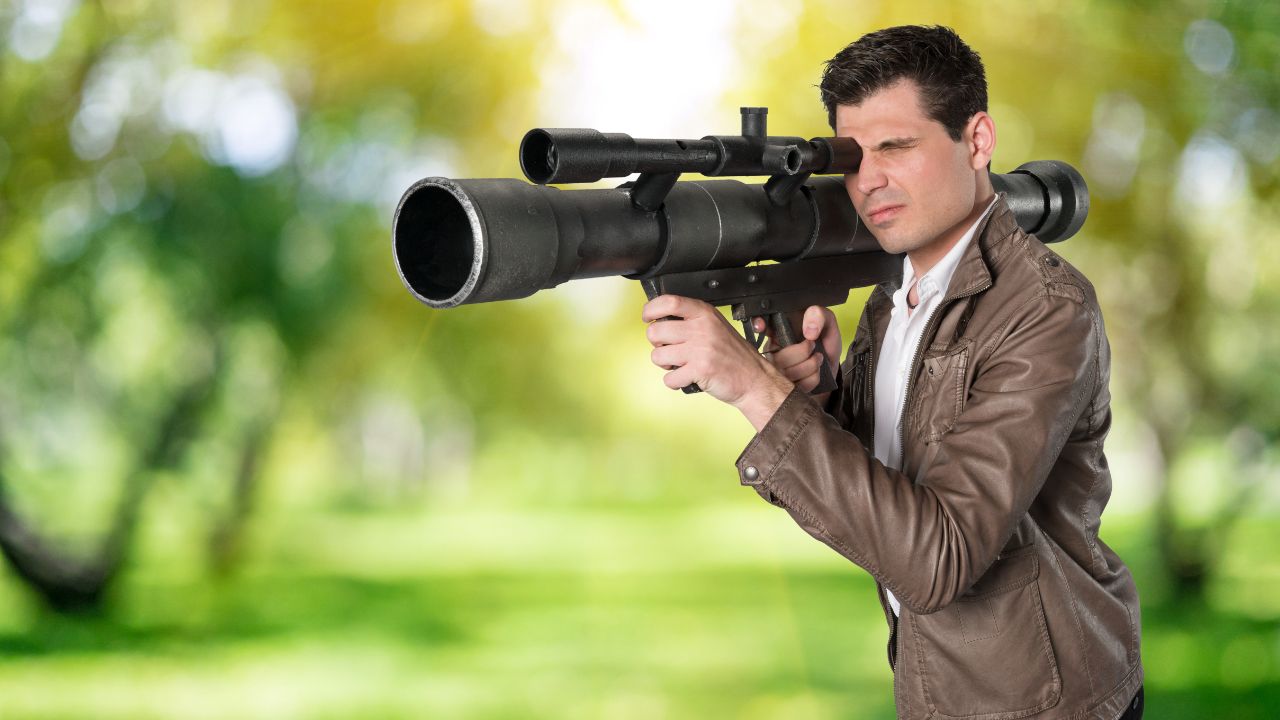 Mann in Lederjacke zielt mit einer Panzerfaust. Im Hintergrund verschwommen ein Park.