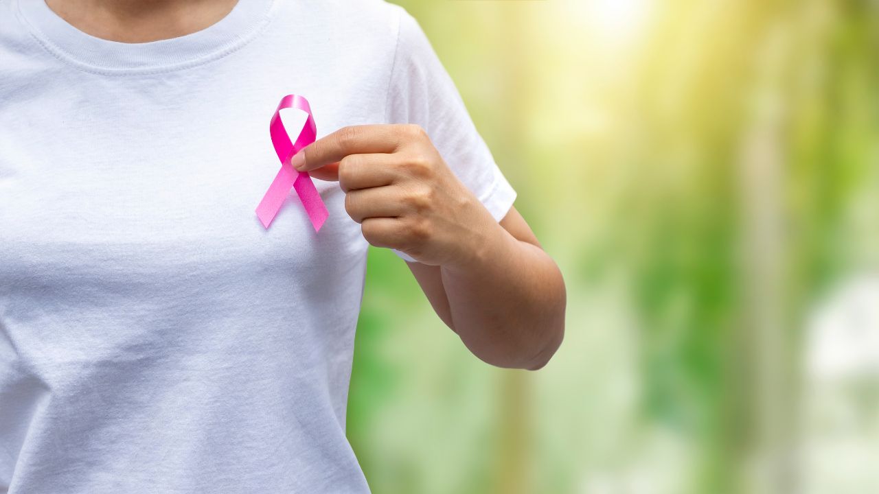 Frau in weißem T-Shirt hält sich eine rosa Krebsschleife vor die Brust.