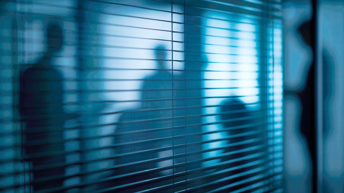 Schemenhafte Personen hinter Jalousien.
