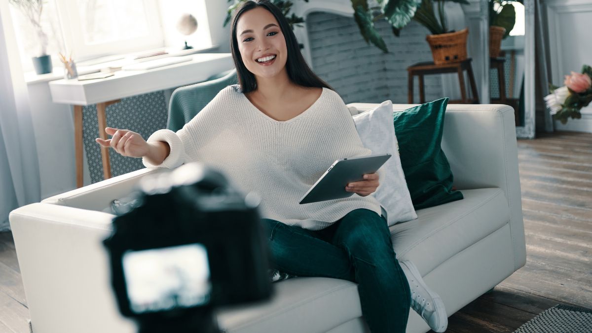 Influencerin sitzt vor laufender Kamera auf weißer Couch.