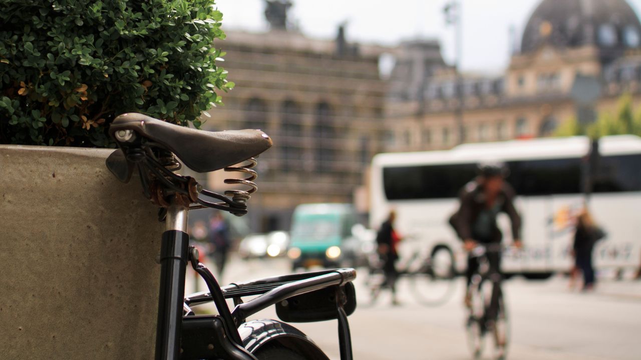 Detail eines Fahrradsattels in der Kopenhagener Innenstadt, während ein Pendler auf einem Fahrrad vorbeifährt.