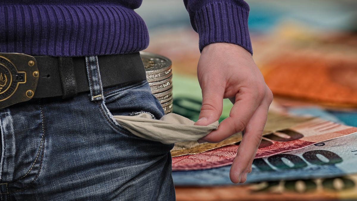 Mann zeigt Innenfutter einer leeren Hosentasche; dahinter Geldscheine und Münzen.
