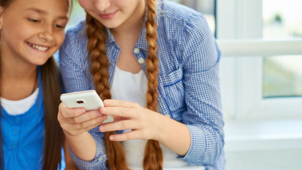 Zwei Mädchen blicken lächelnd auf ein Smartphone-Display.