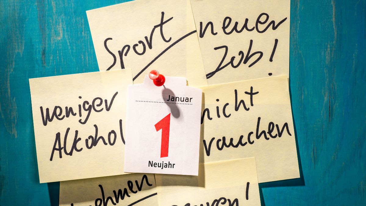 Kalenderblatt 1. Januar mit Zetteln, auf denen Neujahrsvorsätze stehen, wie 'weniger Alkohol' und 'nicht rauchen'