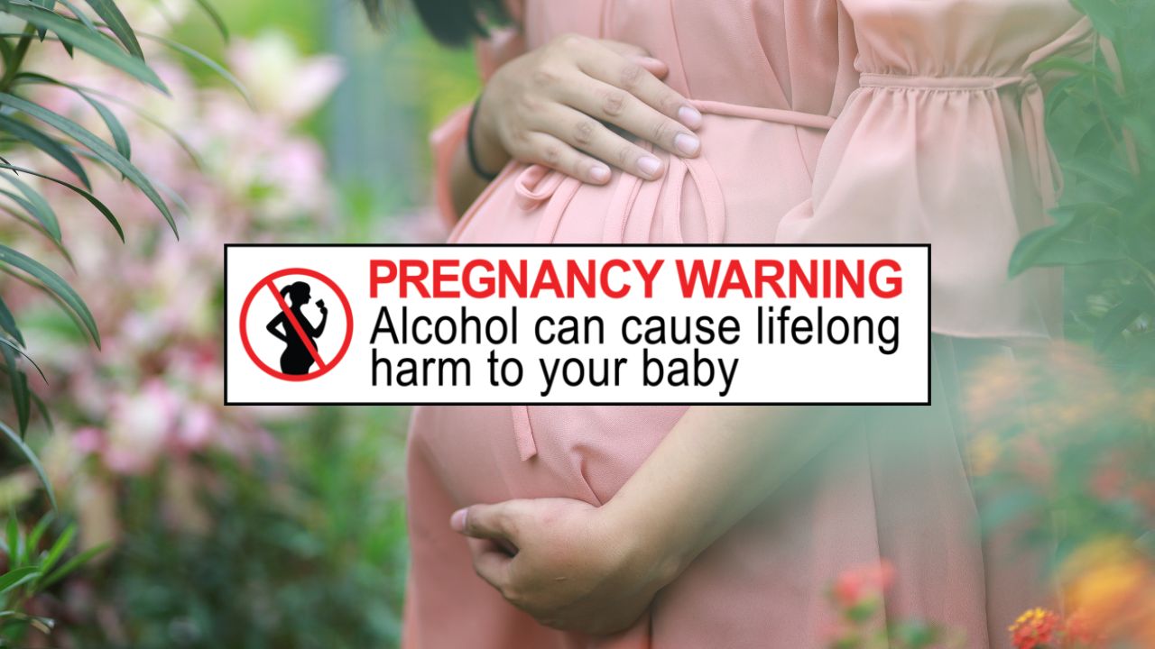 Frau in rosa Kleid hält sich den schwangeren Bauch. Davor das Etikett mit der Warnung vor Alkoholkonsum für Schwangere, wie es in Australien und Neuseeland gesetzlich vorgeschrieben ist.
