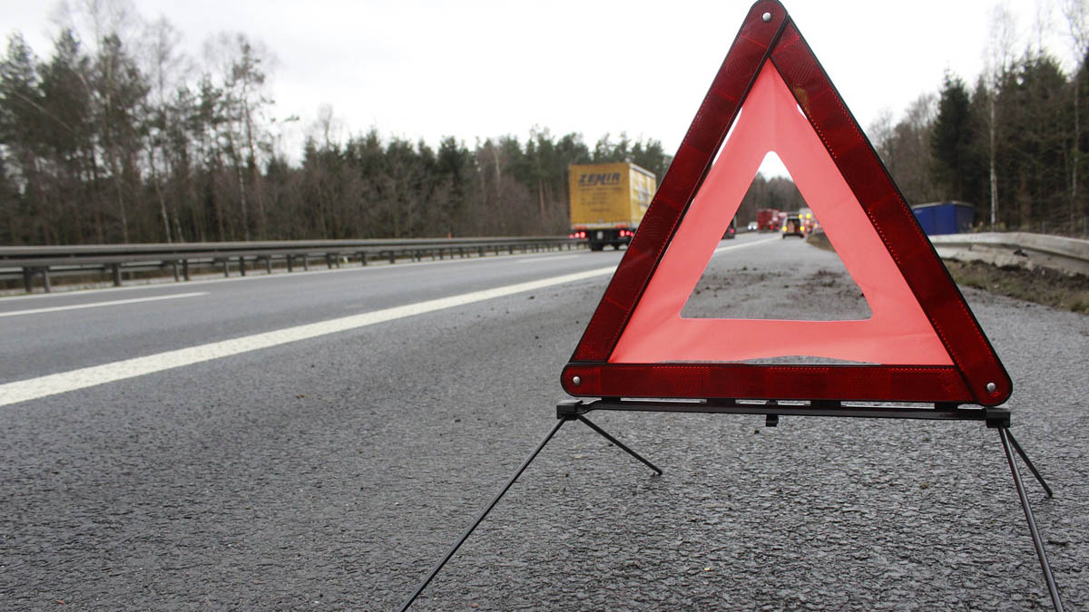 Warndreieck im Vordergrund vor entfernter Unfallszene im Hintergrund.