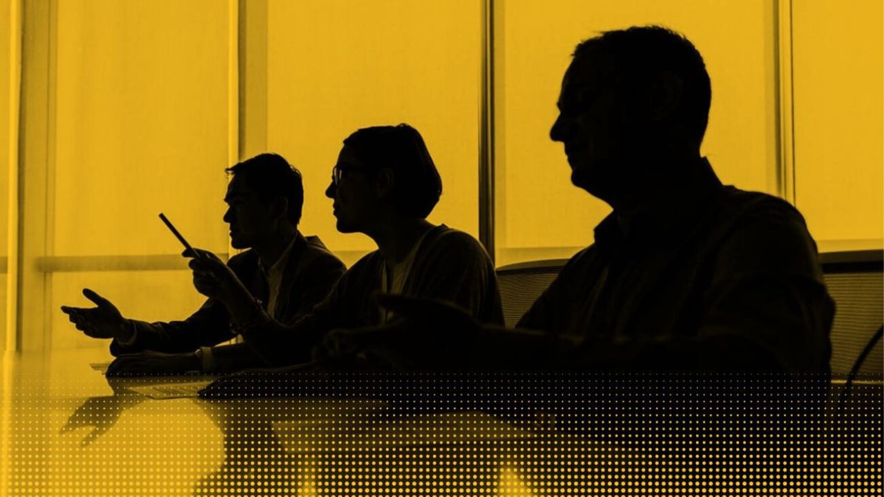 Silhouetten von drei Personen am einem Konferenztisch vor gelbem Hintergrund.