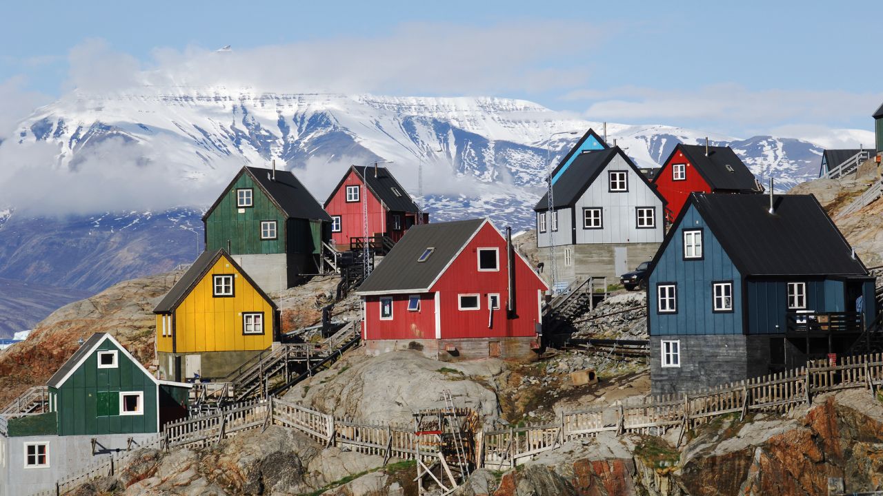 Bunte Häuser auf der Insel Uummannaq, Grönland. Im Hintergrund ist eine Gletscherlandschaft zu sehen. Uummannaq liegt 590 Kilometer nördlich des Polarkreises.