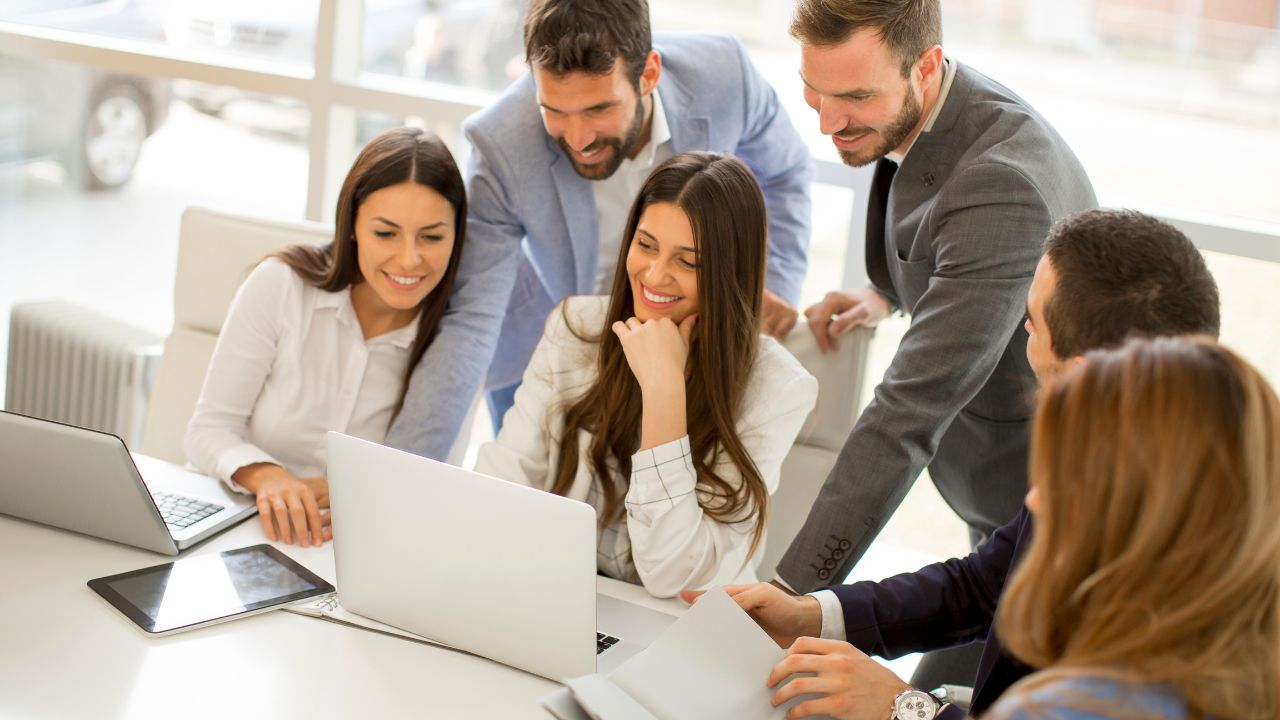 Ein junges Team von Geschäftsleuten schaut erfreut auf den Bildschirm eines Laptops.