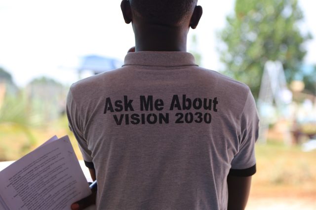 Rückenansicht eines sitzenden Mannes, auf dessen Shirt der Schriftzug 'Ask me about Vision 2030' zu lesen ist.