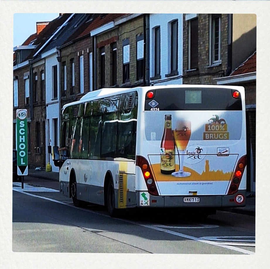 Heckansicht eines weißen Linienbusses der Linie 3 mit Werbung für das Bier 'Brugse Zot - 100% BRUGS' in einer Tempo-30 Schulzone in Belgien.