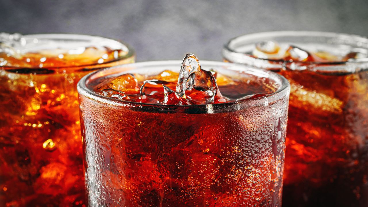 Nahaufnahme von drei Gläsern mit dunklem, kohlensäurehaltigem Getränk, reichlich Eiswürfeln und deutlichem Kondenswasser an den kalten Glaswänden.