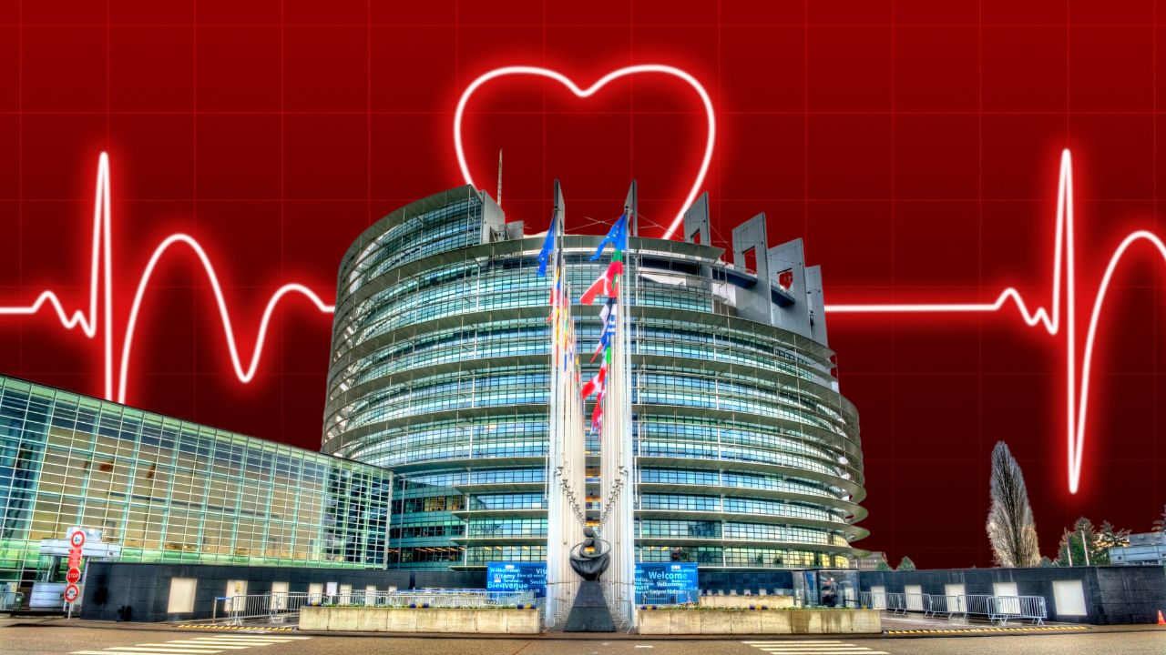 Das moderne, halbrunde Gebäude des Europäischen Parlaments in Straßburg mit seiner Glasfassade und den wehenden EU-Mitgliedstaatenflaggen. Im Hintergrund leuchtet auf rotem Grund ein stilisierter Herzschlag-Verlauf (EKG-Linie), der sich zu einem Herzsymbol formt – eine grafische Metapher für europäische Herz-Gesundheitspolitik.