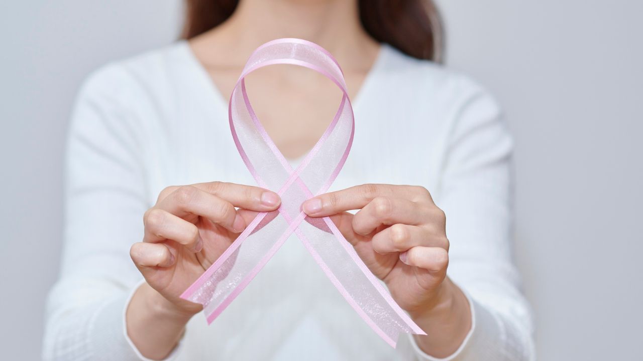 Frau in weißem Oberteil hält eine rosa Schleife als Symbol für die Brustkrebsvorsorge in den Händen.