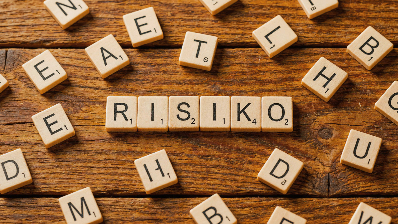 Scrabble-Buchstabensteine auf einem rustikalen Holzuntergrund, in der Mitte bilden sechs Steine das Wort 'RISIKO', umgeben von zufällig verstreuten weiteren Buchstaben.