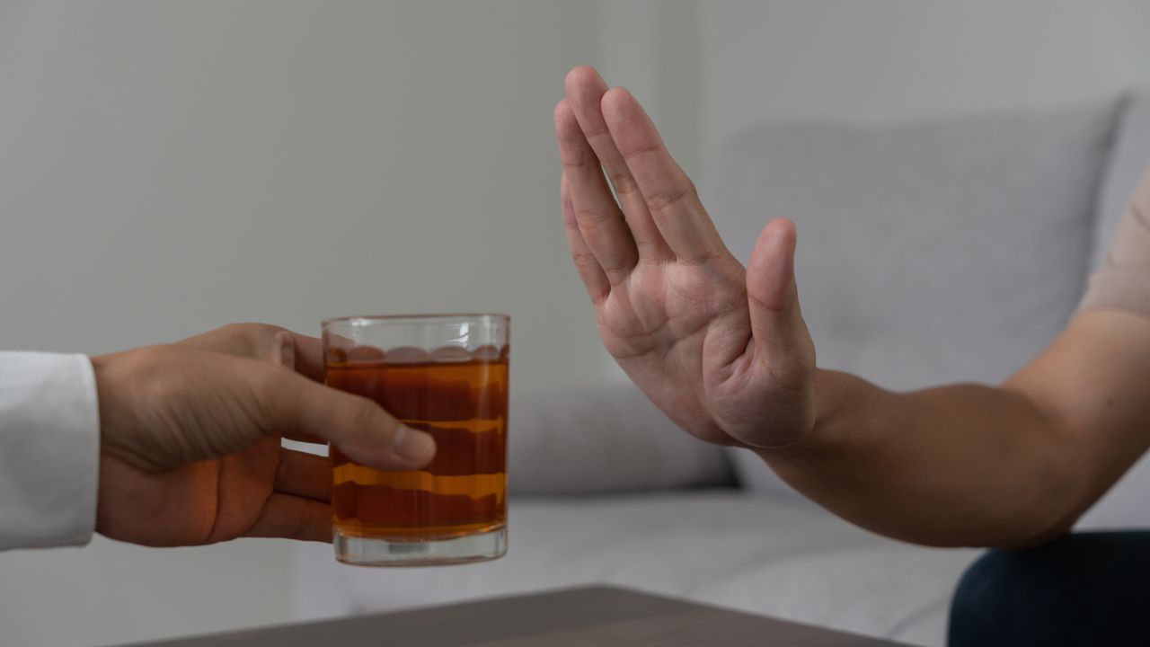 Eine Hand lehnt mit eindeutiger Geste ein angebotenes Glas mit einem alkoholischen Getränk ab.