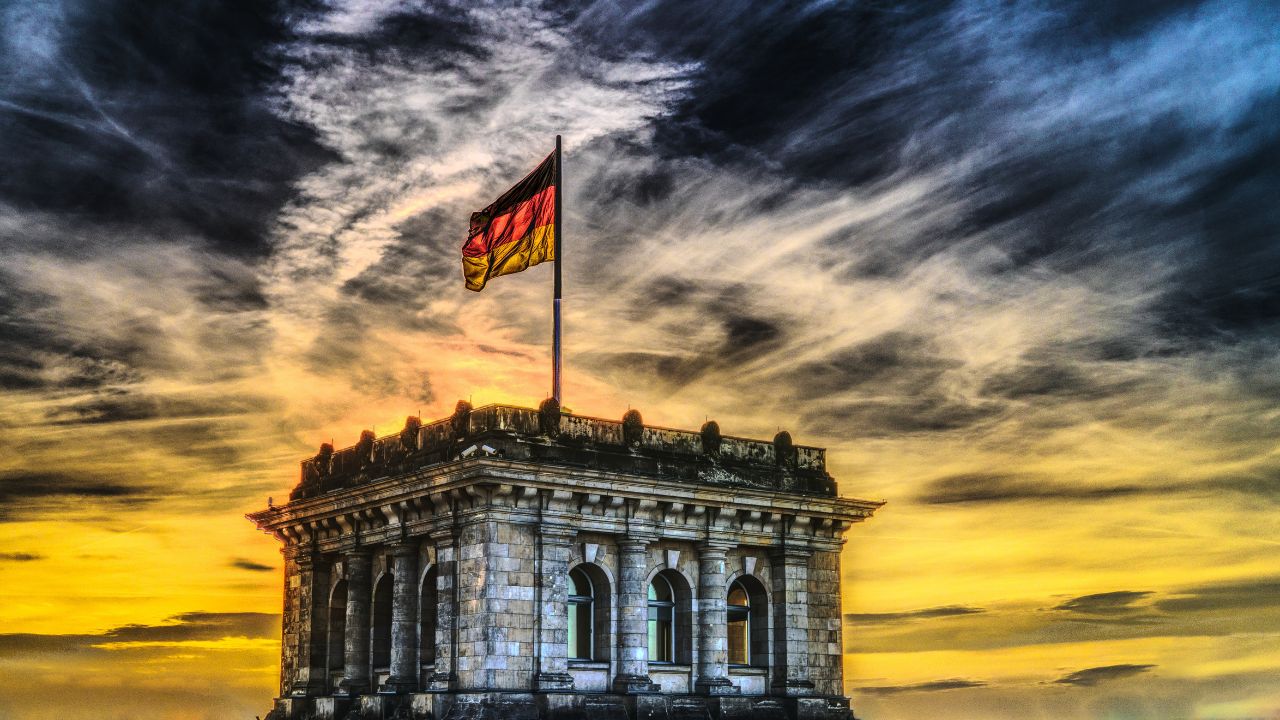 Dramatisch verfremdete Ansichht der deutschen Flagge auf dem Reichstag unter schwarz-gelbem Wolkenhimmel.