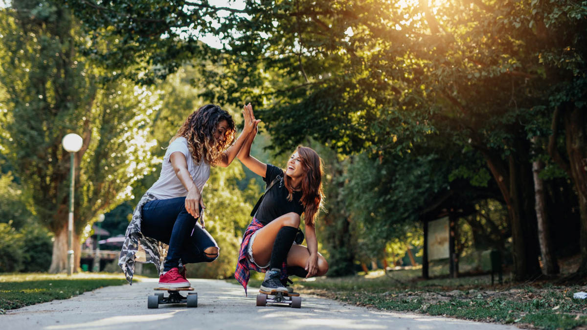 Zwei Mädchen auf Skateboard hockend klatschen sich gegenseitig die Hände