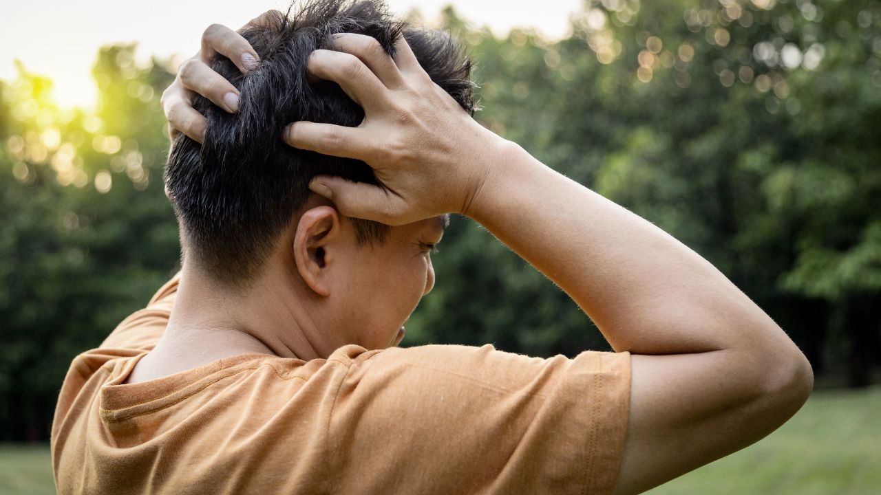 Junger Mann, der sich den schmerzenden Kopf hält.