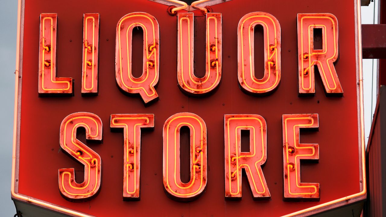 Retro-Neon-Schild eines Spirituosenladens: Rotes Hintergrundschild mit leuchtend orangen Neonröhren, die die 3D-Buchstaben LIQUOR in der ersten Zeile und STORE in der zweiten Zeile umrahmen, im klassischen US-amerikanischen Ladenstil.