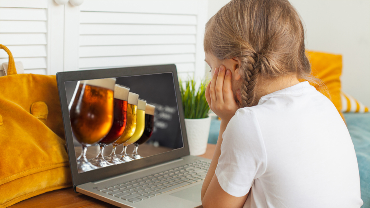 Mädchen sitzt vor dem Bildschirm eines Laptops, auf dem gefüllte Biergläser zu sehen sind.