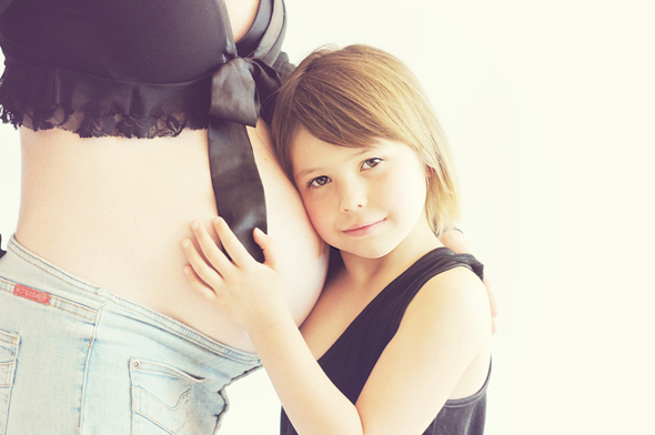 Mädchen schmiegt sich an den Bauch einer schwangeren Frau