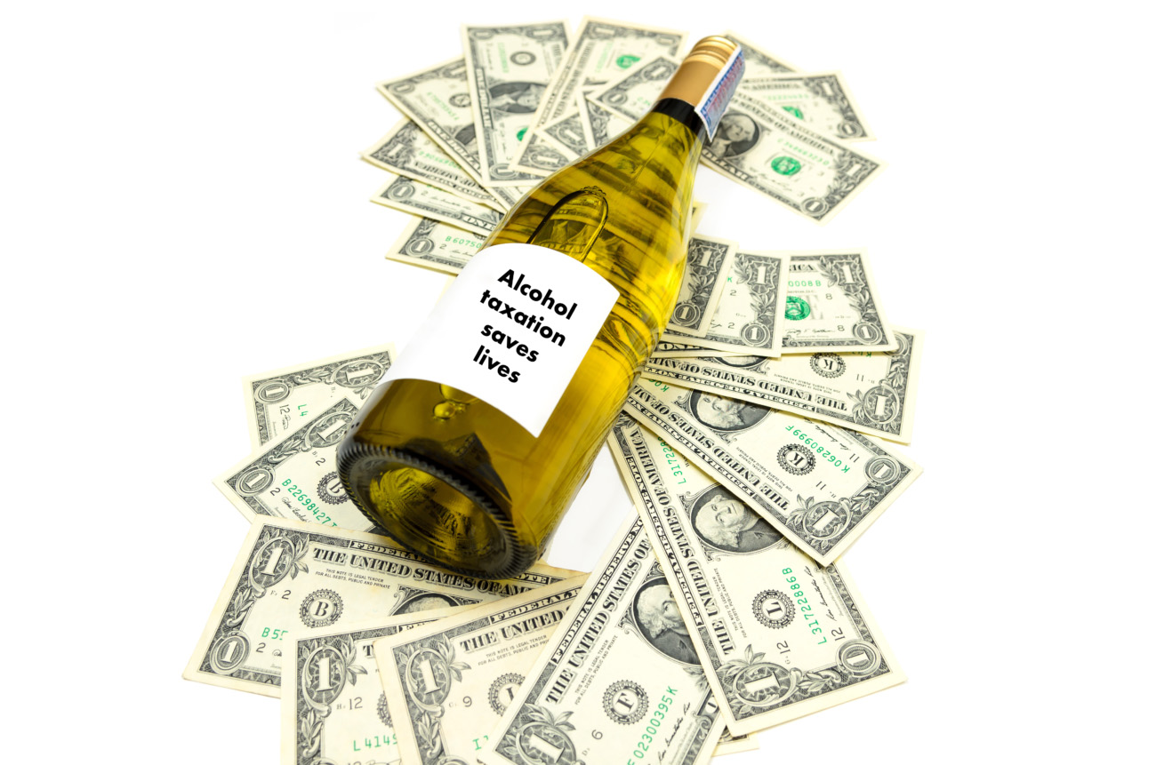 Weinflasche auf Dollarscheinen mit Aufschrift Alcohol taxation saves lives