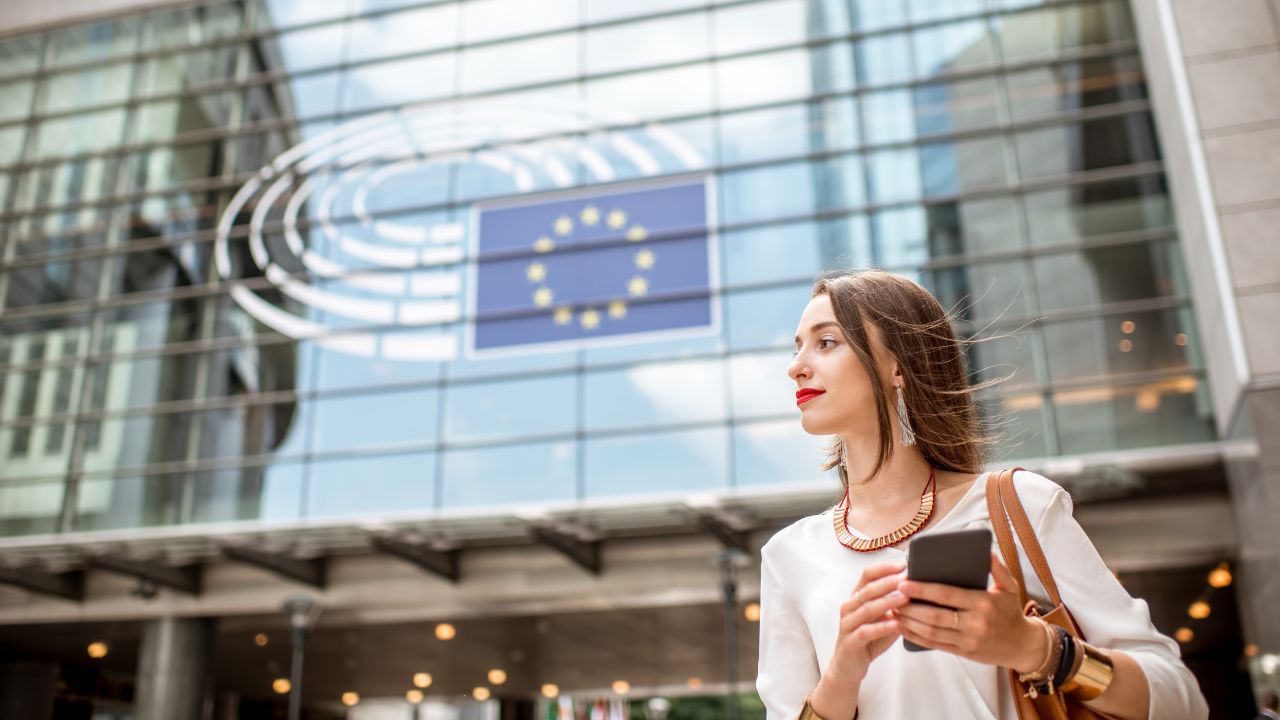Geschäftsfrau in beigem Kostüm vor dem Eingang zum Europäischen Parlament in Brüssel.