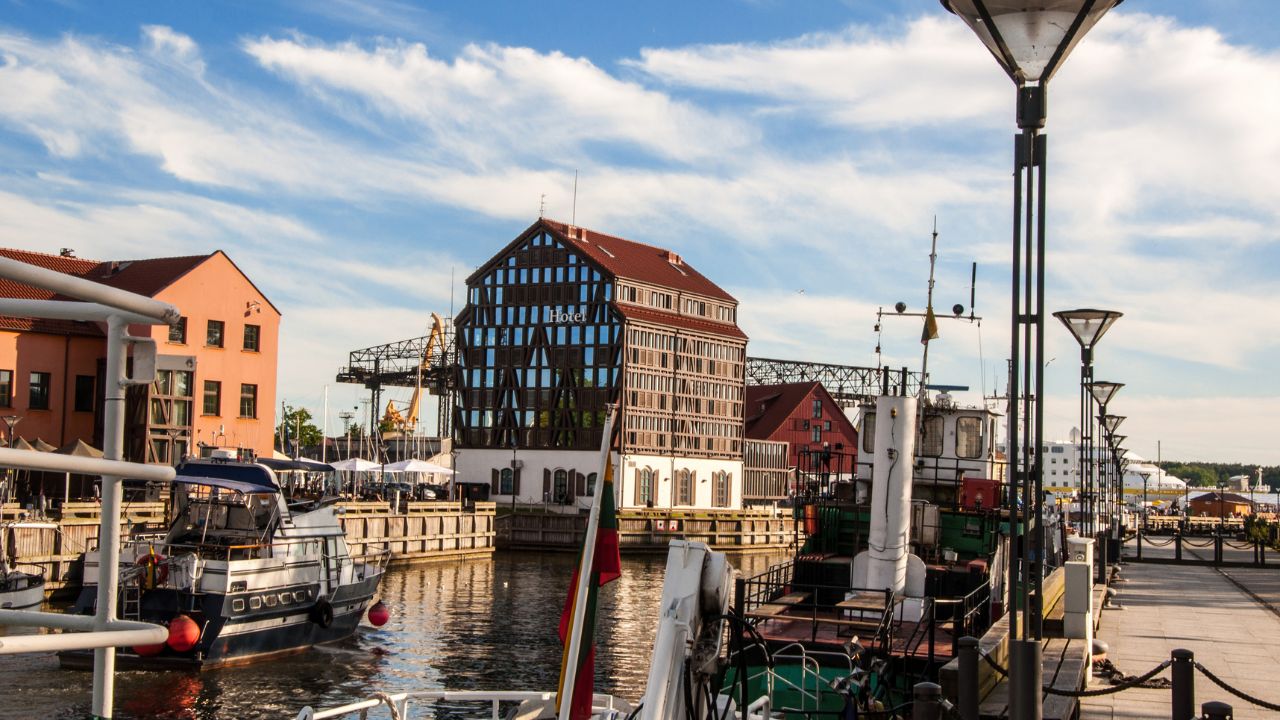Moderner Hafen in Klaipėda mit Blick auf das charakteristische Hotelgebäude, Yachten und die maritime Promenade bei sonnigem Wetter.